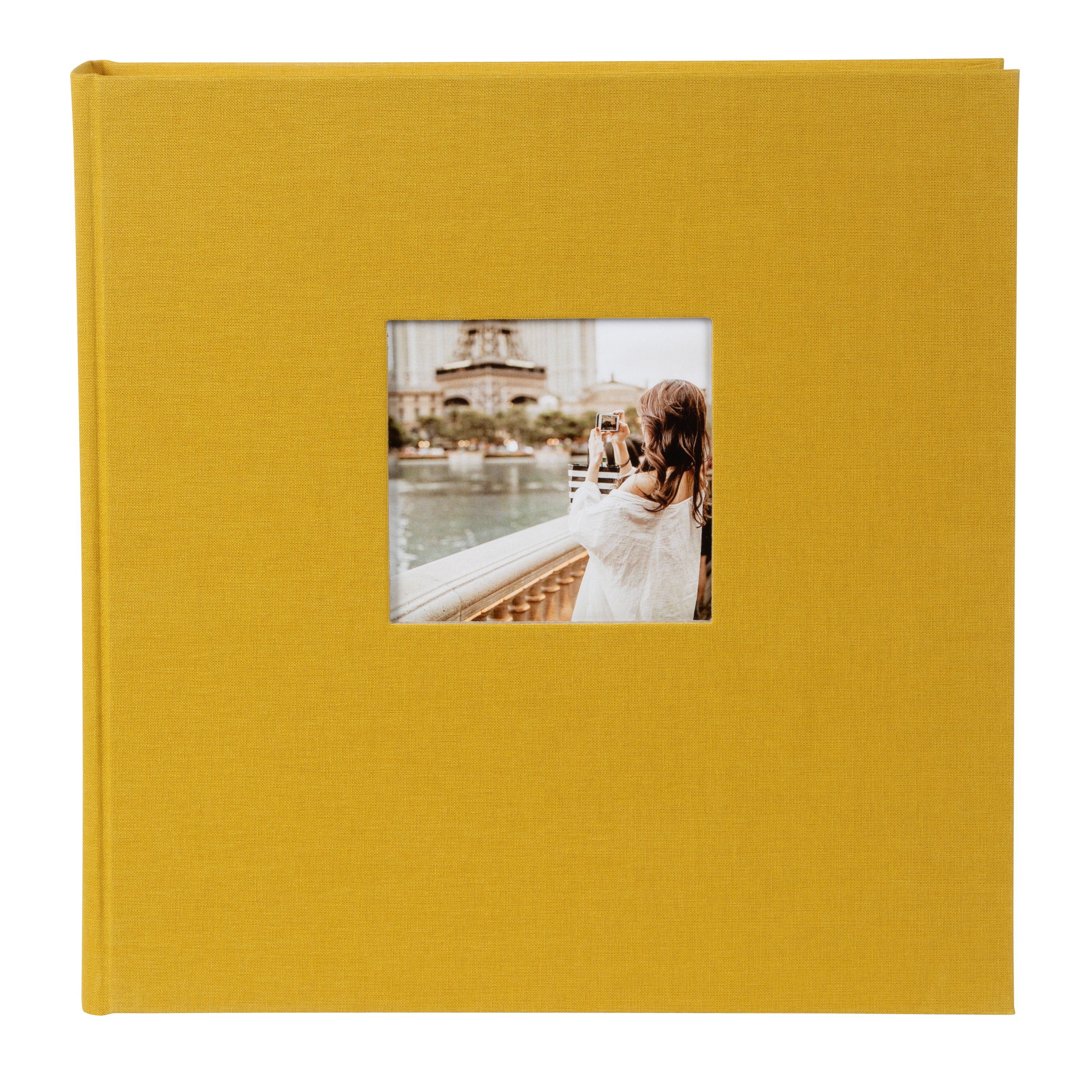 A mustard Goldbuch photo album displays a small cover image of a person with long hair capturing a cityscape, complete with a river and towering structures.