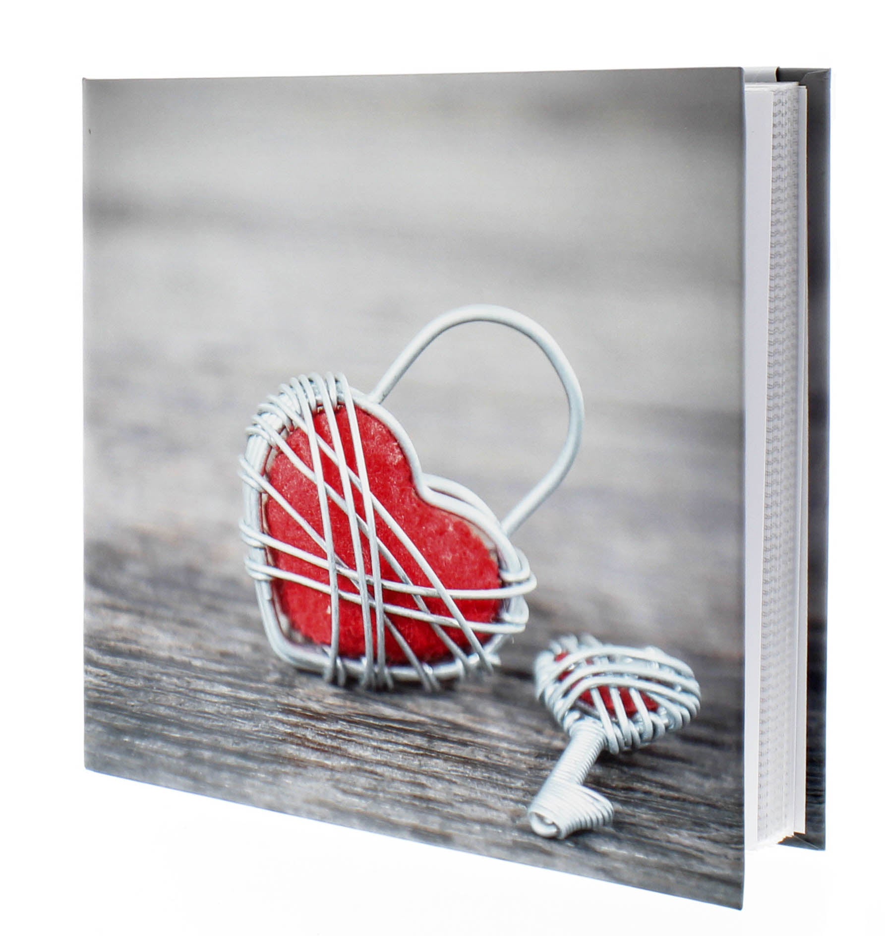 A red heart-shaped key and a wire heart-shaped lock resting on a Hama photo album, representing love and memories.