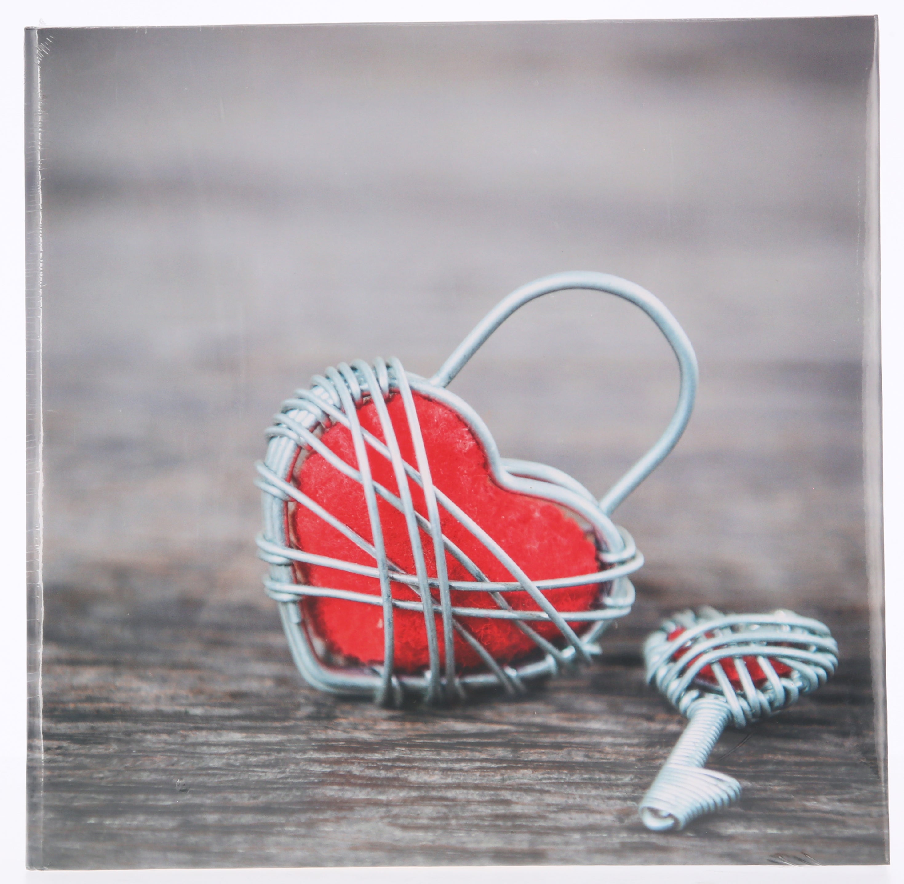 A red heart-shaped key and a wire heart-shaped lock resting on a Hama photo album, representing love and memories.